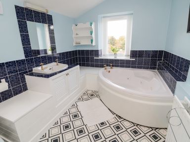 A bathroom with a corner bathtub a sink under a mirror and tiled walls at 19 Duke Street in Alnwick
