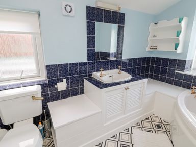 A bathroom with a toilet sink vanity mirror bathtub and wall shelves at 19 Duke Street in Alnwick
