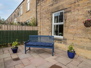 An outdoor patio area with a blue bench and two potted plants against a stone wall at 19 Duke Street in Alnwick