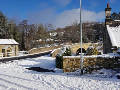A snowy street with a stone bridge and houses surrounded by trees at 19 Duke Street in Alnwick