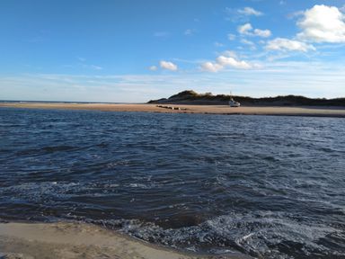 A beach with water in the foreground sand dunes and a boat on the shore at 19 Duke Street in Alnwick