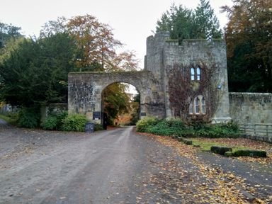 A stone gatehouse with an archway over a dirt road surrounded by trees and shrubs at 19 Duke Street in Alnwick