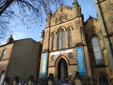 The exterior of a stone building with arched windows and entrance with museum and gallery banners at 19 Duke Street in Alnwick