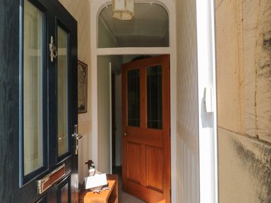An open black front door showing a hallway with a wooden door and a small wooden bench with a decorative bird at 19 Duke Street in Alnwick