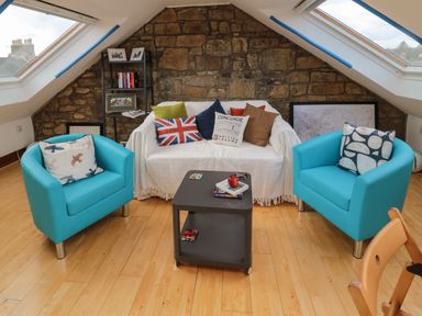 A sitting area with two blue armchairs a white-covered sofa with cushions a small black table wooden floor and skylight windows at 19 Duke Street in Alnwick