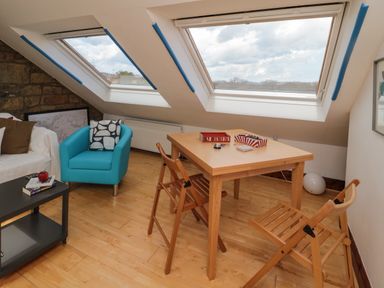 A room with a wooden table and chairs under skylight windows with a blue armchair and a white sofa at 19 Duke Street in Alnwick