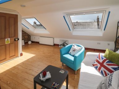 An attic room with slanted windows a blue armchair a white sofa with cushions and a small black table at 19 Duke Street in Alnwick