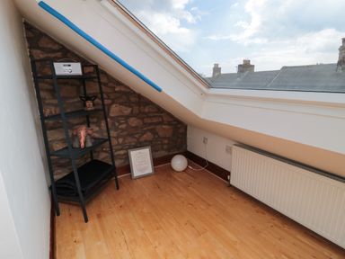 A room with a slanted ceiling window, a black shelf with a radio and decorative items, a framed picture on the floor, and a radiator at 19 Duke Street in Alnwick