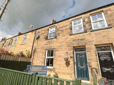 Stone terraced houses with front doors and windows a green fence and a blue bench outside at 19 Duke Street in Alnwick
