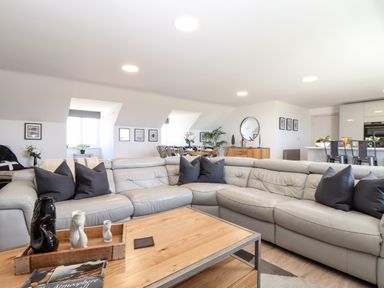 A living room with a grey sectional sofa black pillows wooden coffee table and dining area in the background at Penthouse 23 in Newquay