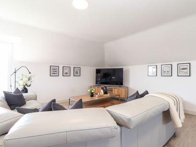 A living room with gray sofas a wooden coffee table a TV on a wooden stand wall art and a floor lamp at Penthouse 23 in Newquay