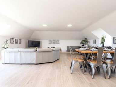 A living area with a large white sectional sofa a dining table with metal chairs and a television on a stand at Penthouse 23 in Newquay