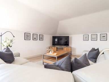 A living room with a white sectional sofa gray pillows a wooden coffee table a flat screen tv on a wooden stand and framed fish artwork on the walls at Penthouse 23 in Newquay