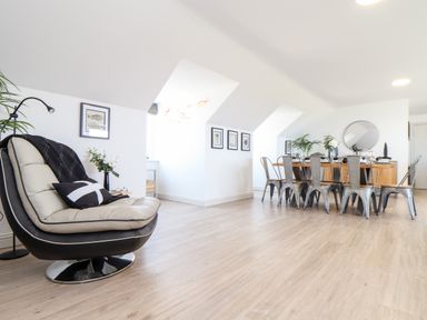 A dining area with a wooden dining table and metal chairs and a lounge chair with a cushion and blanket at Penthouse 23 in Newquay