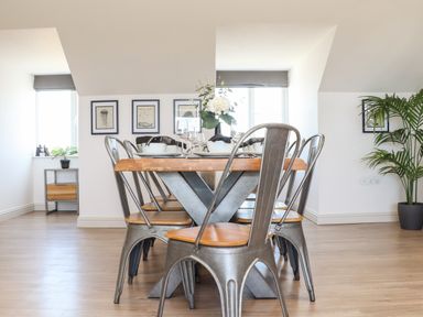 A dining table with metal chairs and tableware in a room with framed art and plants at Penthouse 23 in Newquay