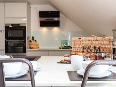 A kitchen with a white table set with cups and bowls a wicker basket and jars on the counter at Penthouse 23 in Newquay