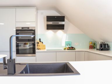 A modern kitchen with a black sink and faucet cutting boards oven toaster and a cookbook on the counter at Penthouse 23 in Newquay