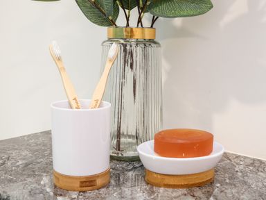 Two wooden toothbrushes in a white holder next to a bar of orange soap on a dish with a glass vase with green leaves on a marble surface at Penthouse 23 in Newquay