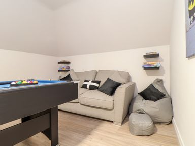 A recreational room with a pool table gray sofa bean bag and shelves with board games at Penthouse 23 in Newquay