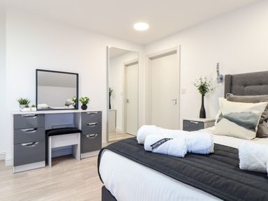 A bedroom with a bed with pillows and towels a vanity table with a mirror a chair and plants at Penthouse 23 in Newquay