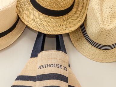 A wall with three straw hats and a striped bag that says Penthouse 23