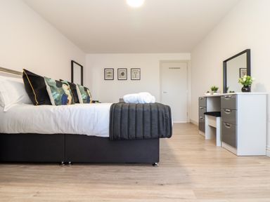 A bedroom with a bed with pillows and towels a dressing table with a mirror and plants and framed pictures on the wall at Penthouse 23 in Newquay