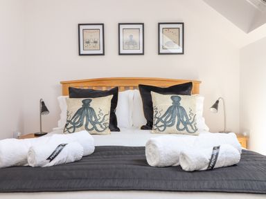 A bed with octopus print pillows white rolled towels and framed sea creature pictures on the wall at Penthouse 23 in Newquay