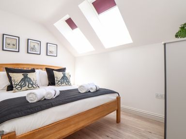 A bedroom with a wooden bed frame pillows with octopus designs and three skylight windows at Penthouse 23 in Newquay