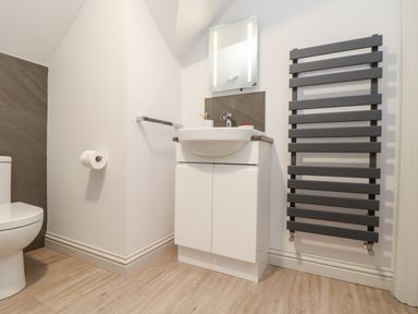 A bathroom with a white toilet a sink with cabinet a mirror and a black towel radiator at Penthouse 23 in Newquay
