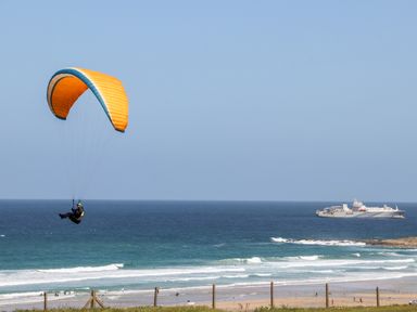 A person paragliding over the ocean with a large ship in the distance at Penthouse 23 in Newquay