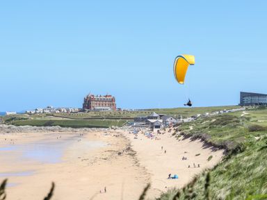 A sandy beach with people and a person paragliding above near buildings and grassy dunes at Penthouse 23 in Newquay