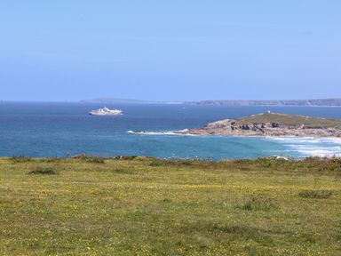 A coastal landscape with grass in the foreground a rocky peninsula and a ship on the sea at Penthouse 23 in Newquay