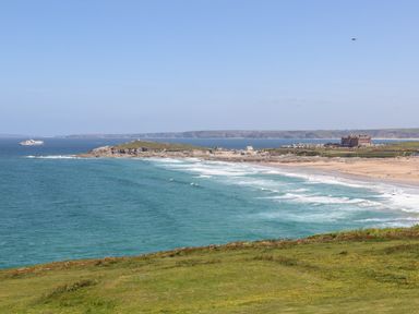 A coastal landscape with green grass in the foreground a beach with waves and buildings in the background at Penthouse 23 in Newquay