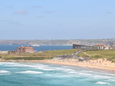 A beach with people near ocean waves with buildings and cliffs in the background at Penthouse 23 in Newquay