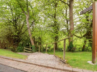 A gravel path with wooden railings leading into a wooded area with a signpost showing directions at 23 Bossiney Bay in Tintagel