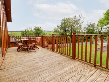 An outdoor wooden deck with a table and chairs surrounded by a wooden railing at 23 Bossiney Bay in Tintagel