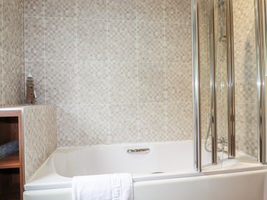 A bathroom with a bathtub shower screen and a towel on the side at 23 Bossiney Bay in Tintagel