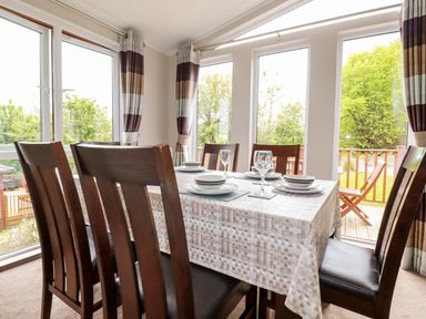 A dining area with a table set for six and large windows with curtains at 23 Bossiney Bay in Tintagel