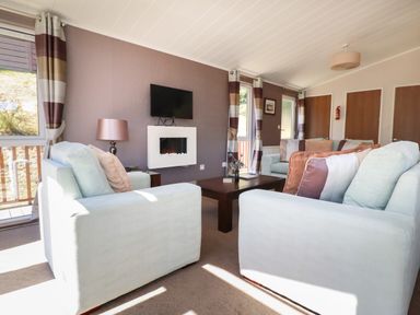 A living room with sofas a coffee table wall mounted tv and electric fireplace at 23 Bossiney Bay in Tintagel