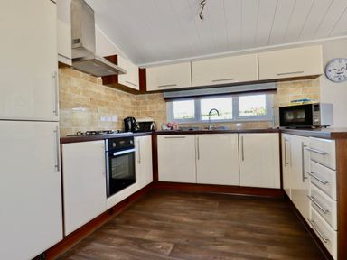 A kitchen with white cabinets a gas stove an oven a microwave kettle and a window at 23 Bossiney Bay in Tintagel