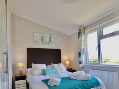 A bedroom with a bed folded towels on a teal runner two bedside tables with lamps and a window at 23 Bossiney Bay in Tintagel