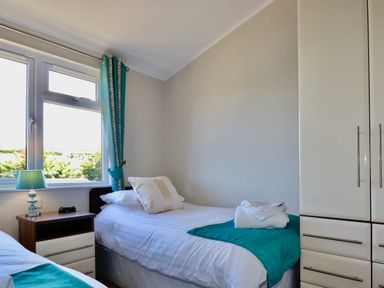 A bedroom with two single beds a bedside table and a wardrobe at 23 Bossiney Bay in Tintagel