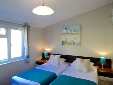 A bedroom with two single beds bedside tables and lamps at 23 Bossiney Bay in Tintagel