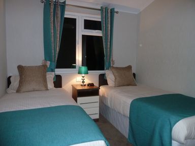 A bedroom with two single beds with teal blankets and a nightstand with a teal lamp at 23 Bossiney Bay in Tintagel