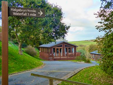 A wooden signpost with directions to Halgabron and waterfall near wooden houses among trees and grassy hills at 23 Bossiney Bay in Tintagel