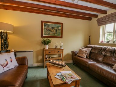 A living room with brown leather sofas a wooden coffee table with magazines a side table with candles and a painting on the wall at Columbine Cottage in Hawkshead