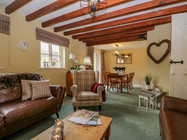 A living room with wooden beams on ceiling leather couches and a beige armchair next to a dining area with wooden chairs at Columbine Cottage in Hawkshead