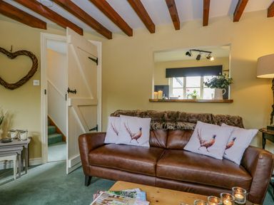A living room with a brown leather sofa and pheasant cushions by a window opening at Columbine Cottage in Hawkshead