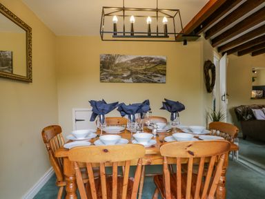 A dining room with a wooden table set with white dishes and glasses under a ceiling light at Columbine Cottage in Hawkshead