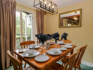 A dining room with a wooden table set with white plates bowls wine glasses and black napkins at Columbine Cottage in Hawkshead